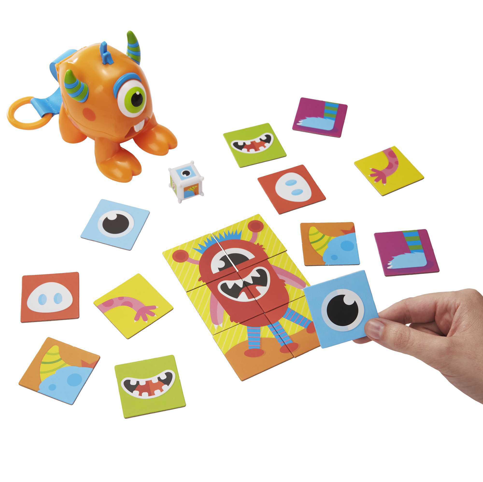 Ein Spielzeugmonster und Puzzleteile. Die Hand hält ein blaues Augenteil zum roten Monsterpuzzle.