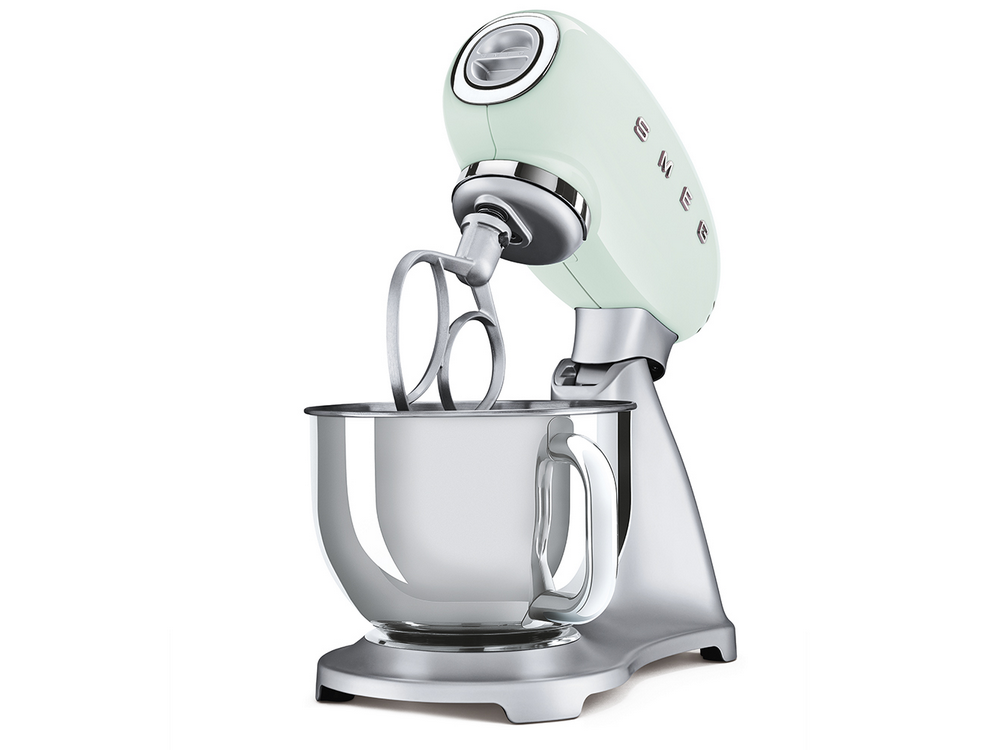 Una batidora Smeg verde menta con un cuenco plateado sobre un fondo blanco. La batidora está encendida.