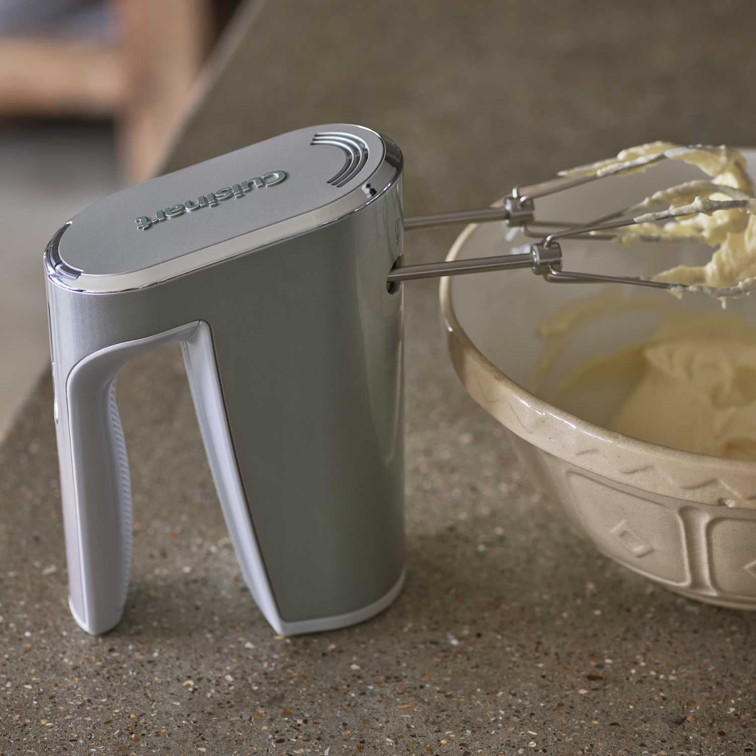 Een handmixer naast een kom met boter. De mixer is grijs, de kom is keramiek.