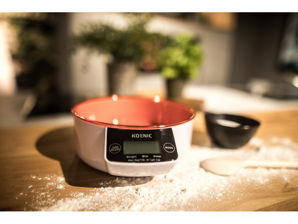 Una báscula blanca con un cuenco rojo, midiendo ingredientes sobre una superficie de madera.