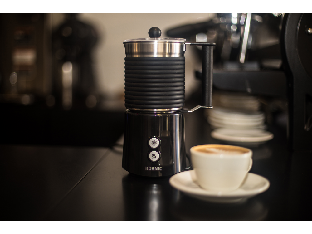 Un espumador de leche negro y plateado con una taza de café en una mesa.