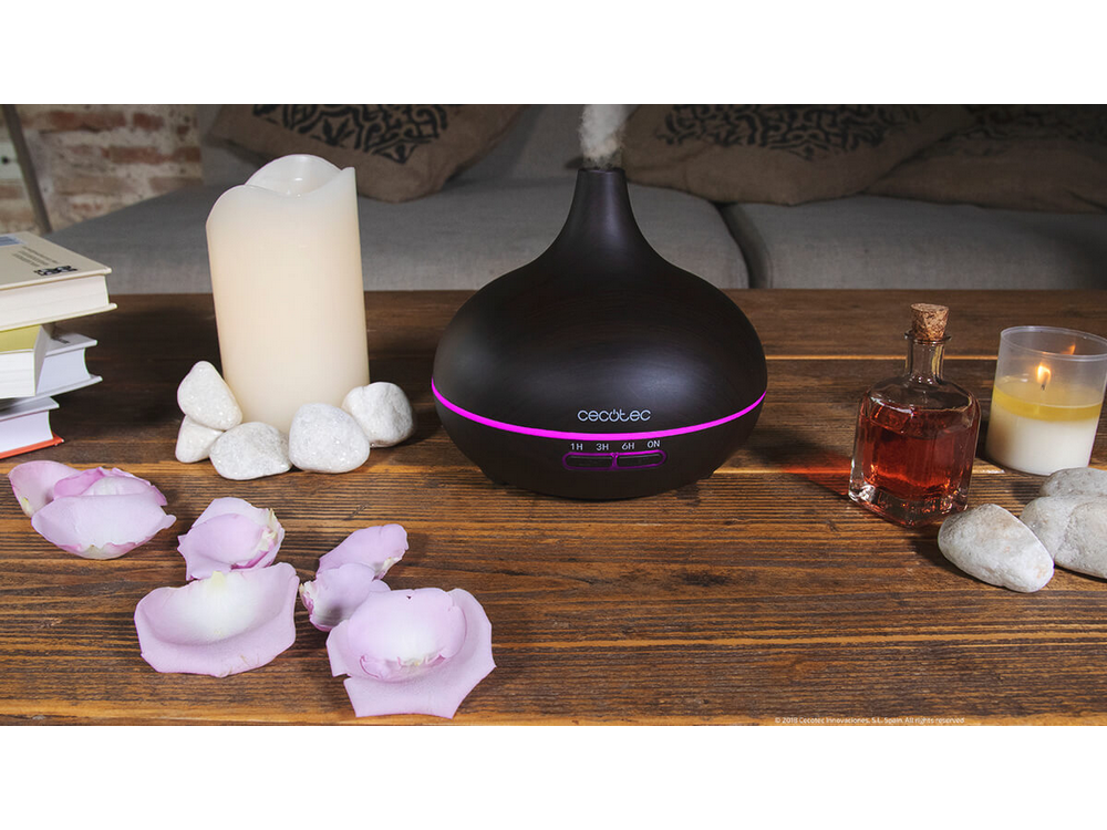 Mesa de madera con difusor negro, vela, pétalos de rosa y libros. Iluminación cálida.