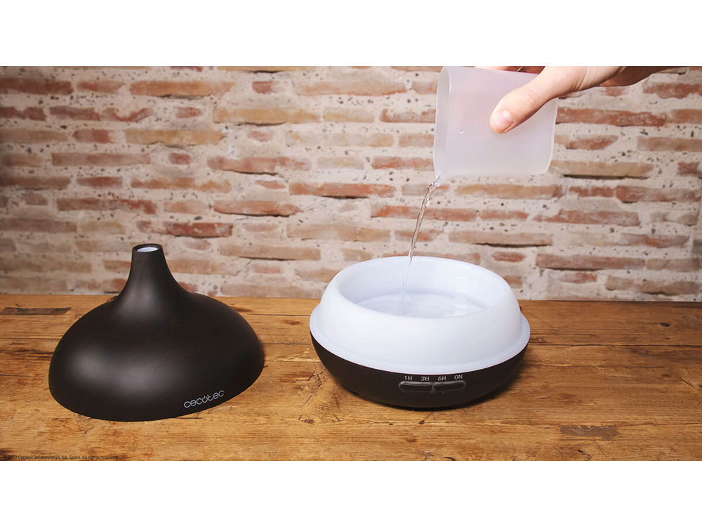 Difusor con base negra y parte superior blanca. Se vierte agua de un recipiente.