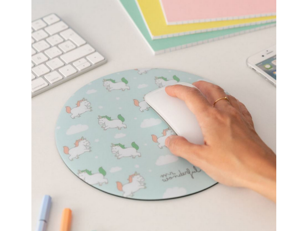 Una mano usando un ratón blanco sobre una alfombrilla con ilustraciones de unicornios en un escritorio.
