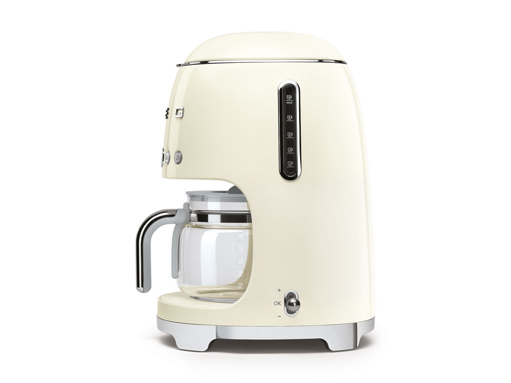 Cafetera Smeg color crema con jarra de vidrio e indicadores de nivel de agua, sobre blanco.
