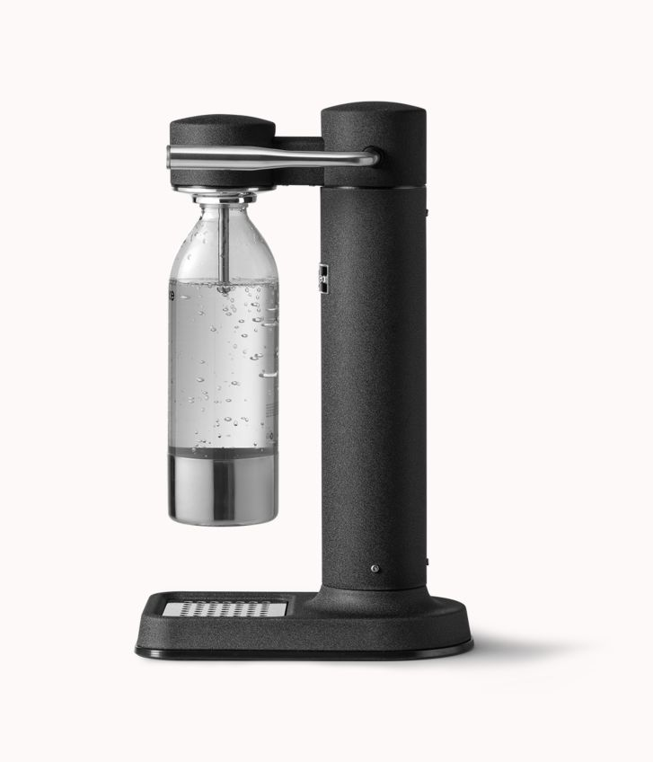 Ein schwarzer Soda-Maker mit einer Wasserflasche darin. Der Hintergrund ist weiß.