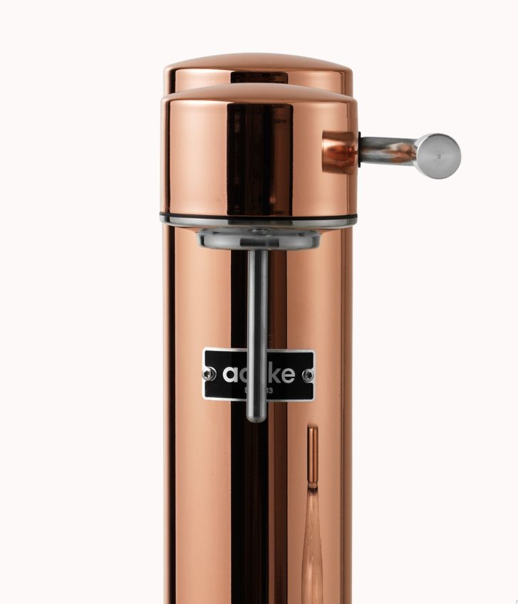 Eine kupferfarbene SodaStream-Maschine. Sie hat einen silbernen Hebel und ein schwarzes Etikett.