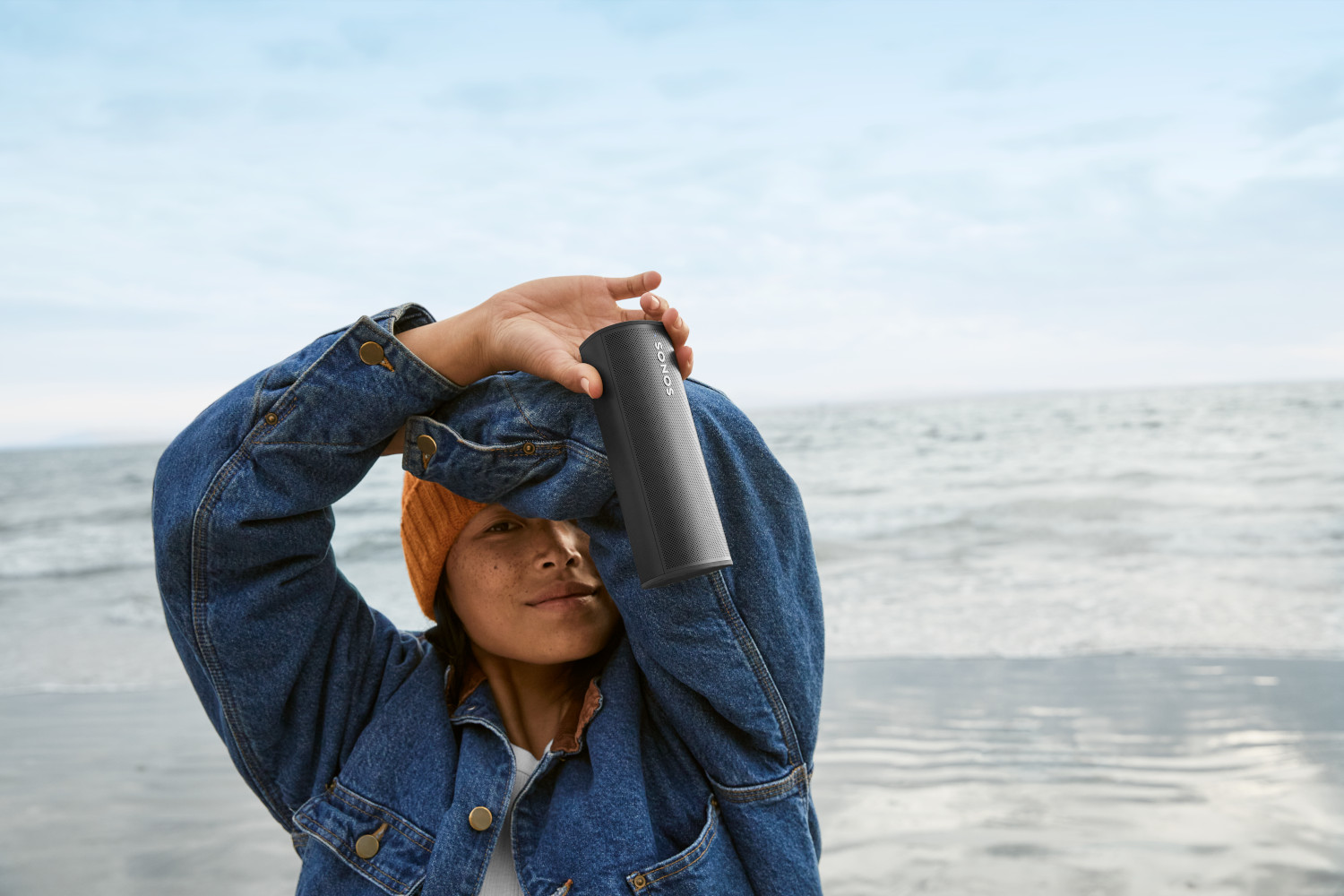 Vrouw houdt een zwarte luidspreker bij haar gezicht op het strand.