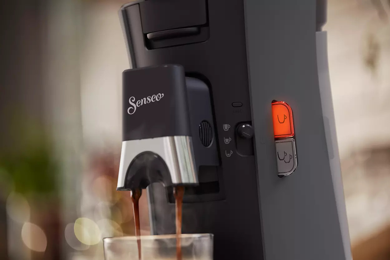 Close-up van een zwarte Senseo koffiemachine die koffie in een glas schenkt.