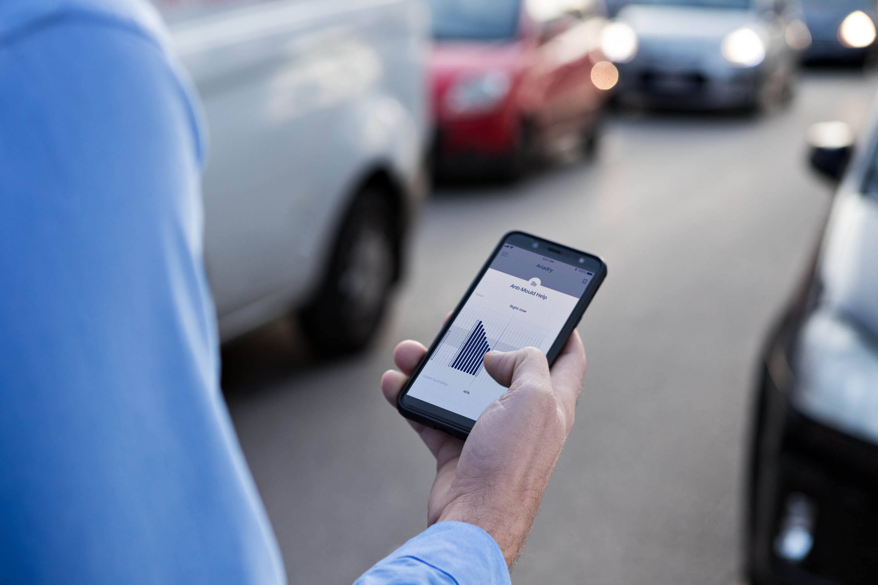 Person hält Smartphone mit App, die Diagramm zeigt, auf Straße mit geparkten Autos.