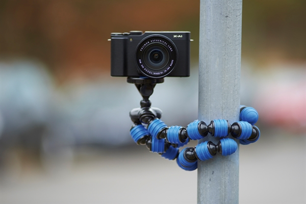 A black camera is mounted on a flexible tripod attached to a metal pole outdoors.
