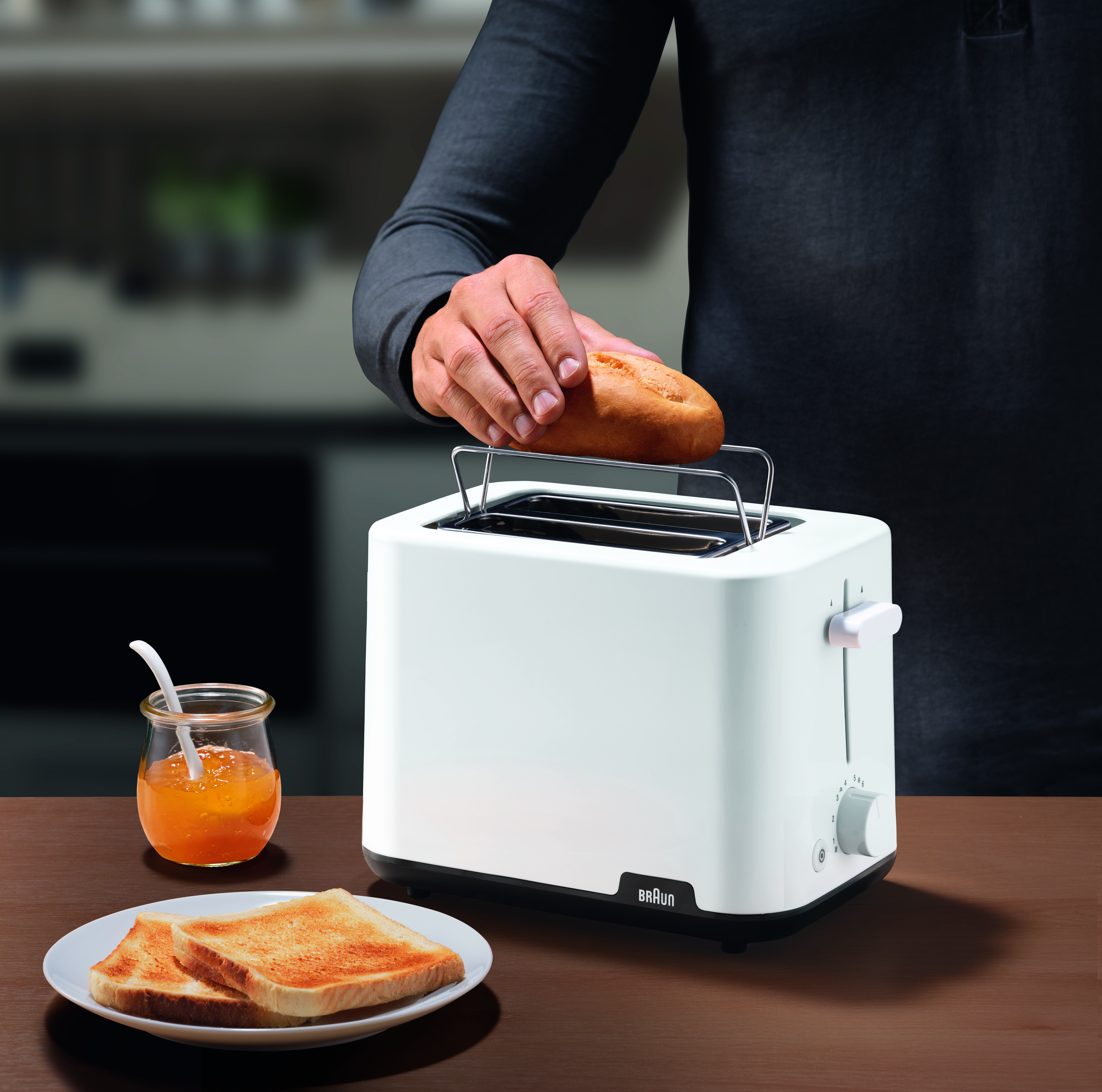 Eine Person, die Brot in einem weißen Toaster toastet, mit Marmelade und Toast.
