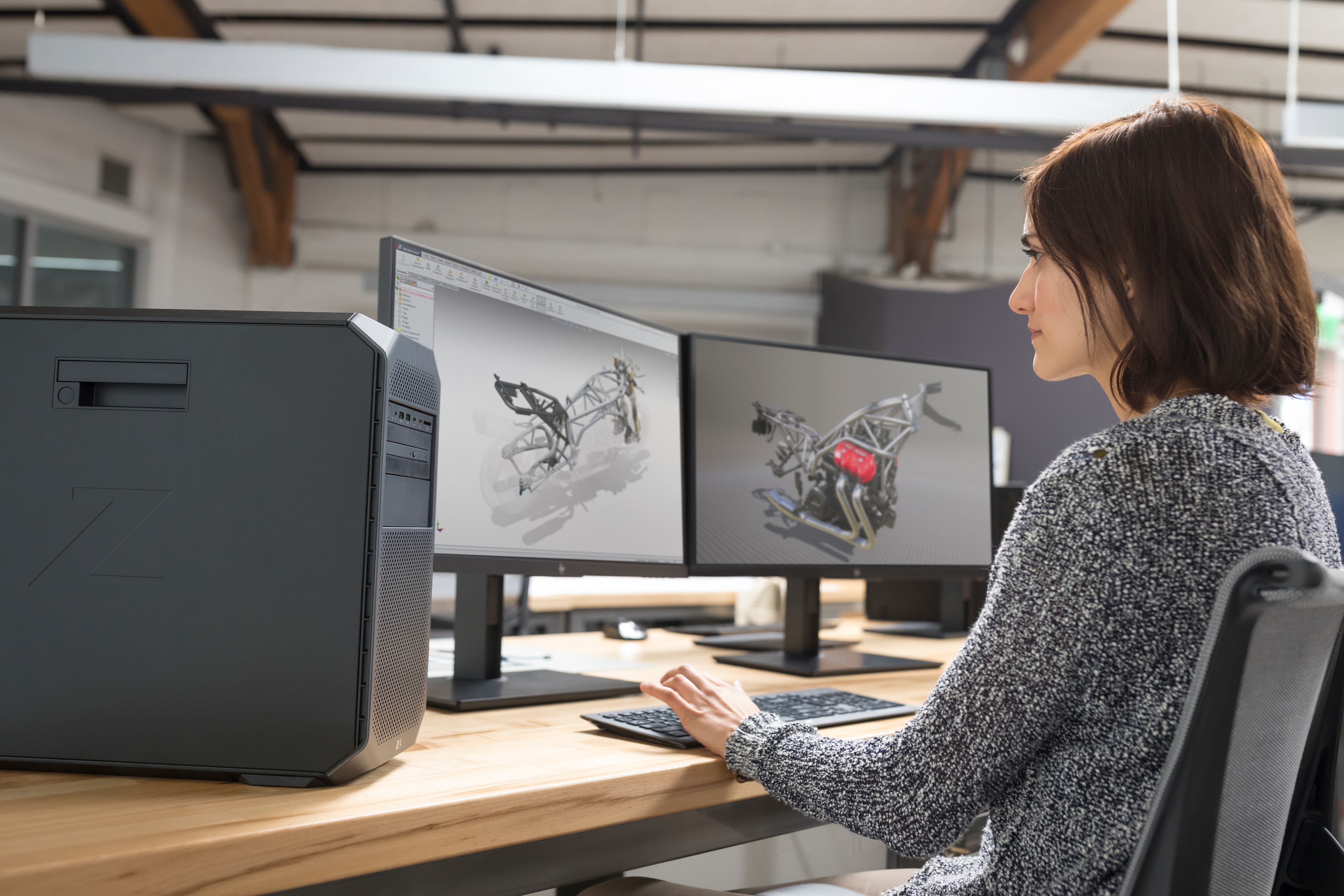 Eine Frau sitzt an einem Schreibtisch und arbeitet an zwei Computerbildschirmen, die Designs anzeigen.