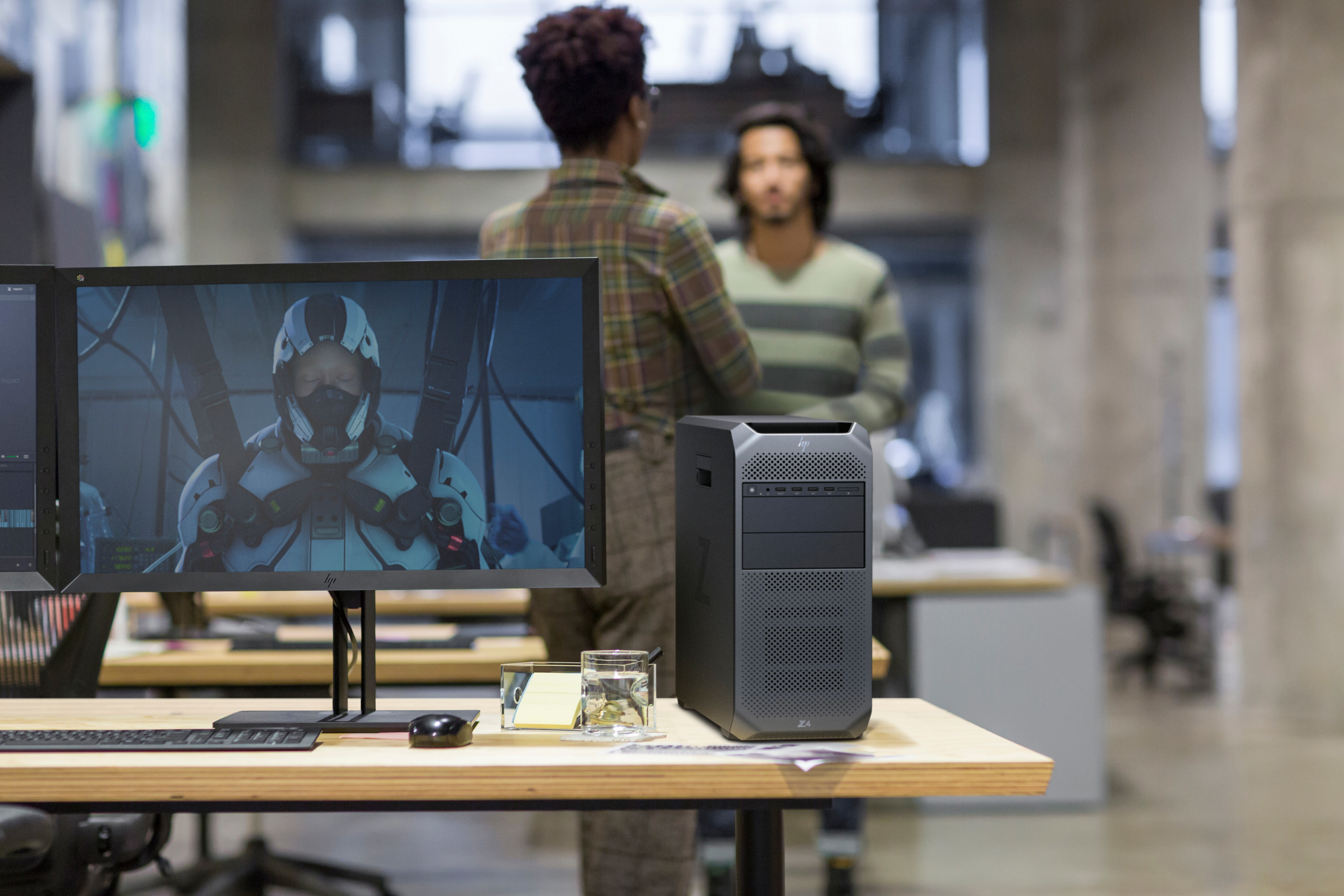 Büroszene mit zwei Personen im Hintergrund. Ein Computermonitor zeigt eine Person in einem Raumanzug.