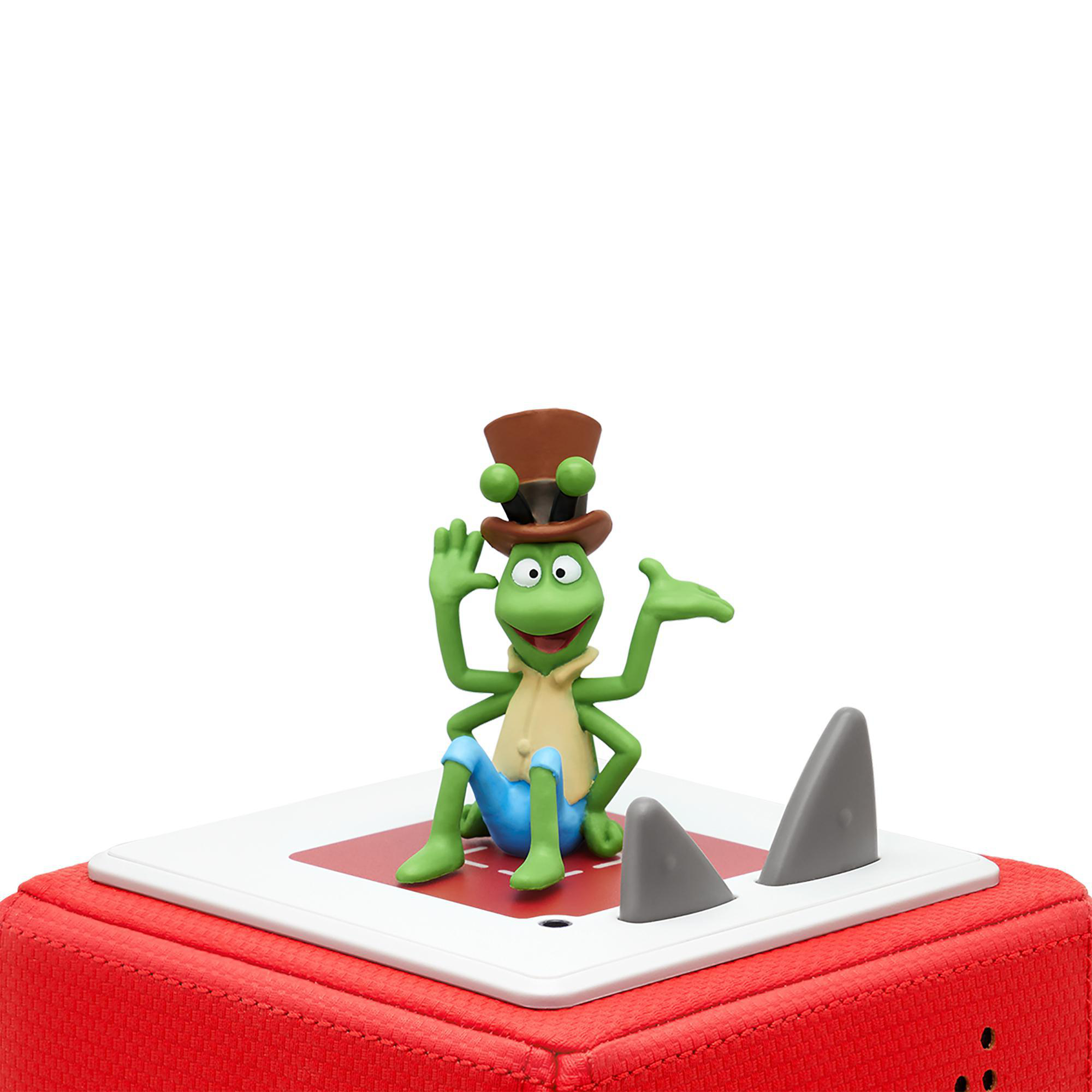 Ein grünes Froschspielzeug mit Zylinder sitzt auf einer roten Box mit grauen Haifischflossen.