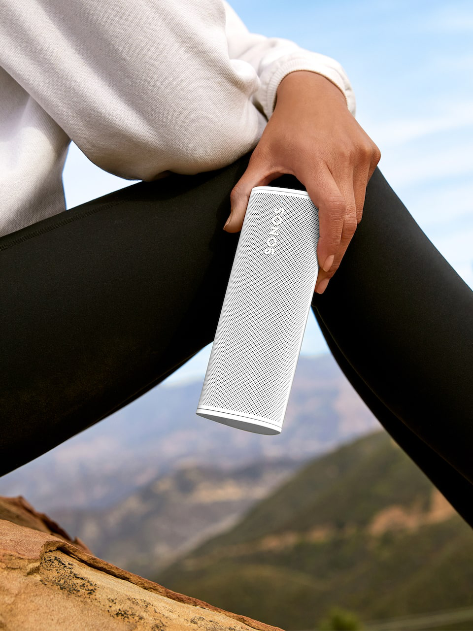 Eine Person hält einen weißen Sonos-Lautsprecher mit Berg-Hintergrund.