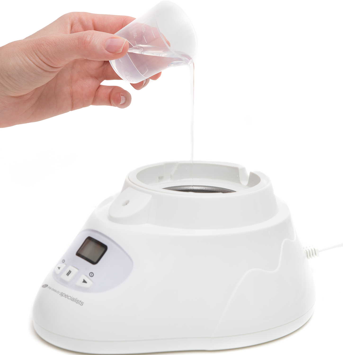 A hand pouring liquid from a measuring cup into a white device.