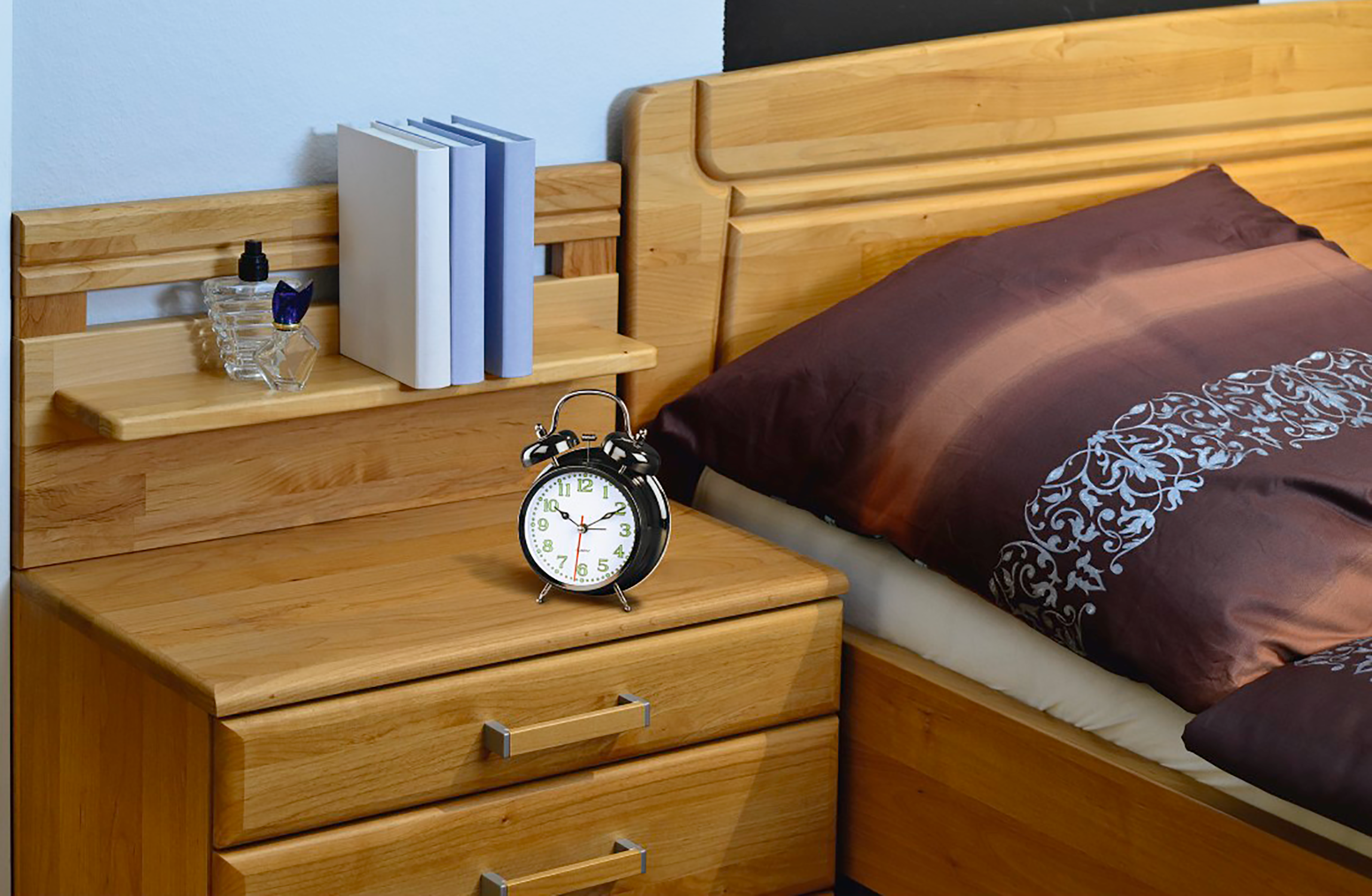 A bedroom scene with a wooden nightstand and bed. A clock and books on the stand.