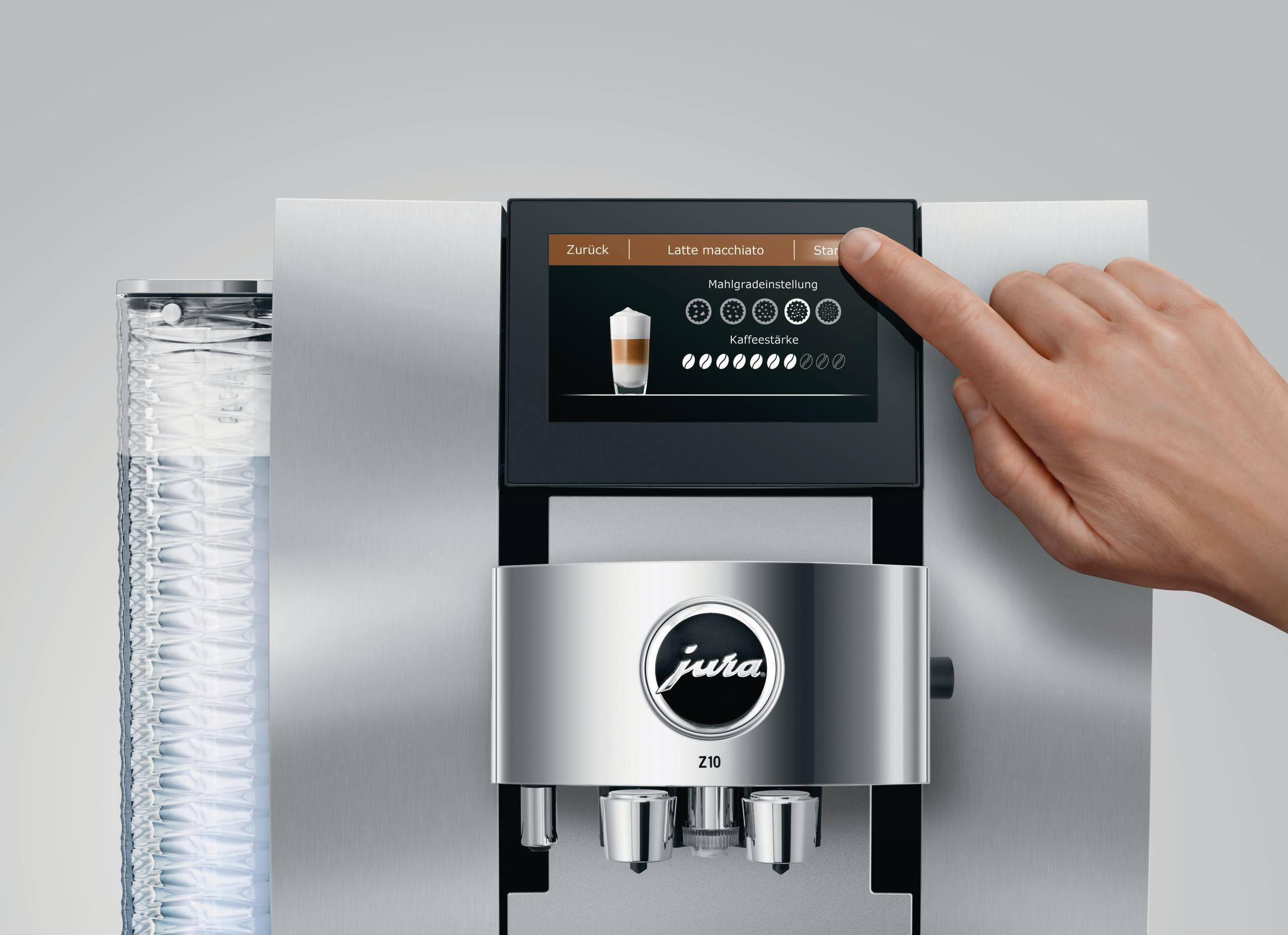 Ein Finger berührt einen Kaffeeautomaten-Bildschirm. Der Bildschirm zeigt Optionen für Kaffeegetränke an. Die Maschine ist silber.