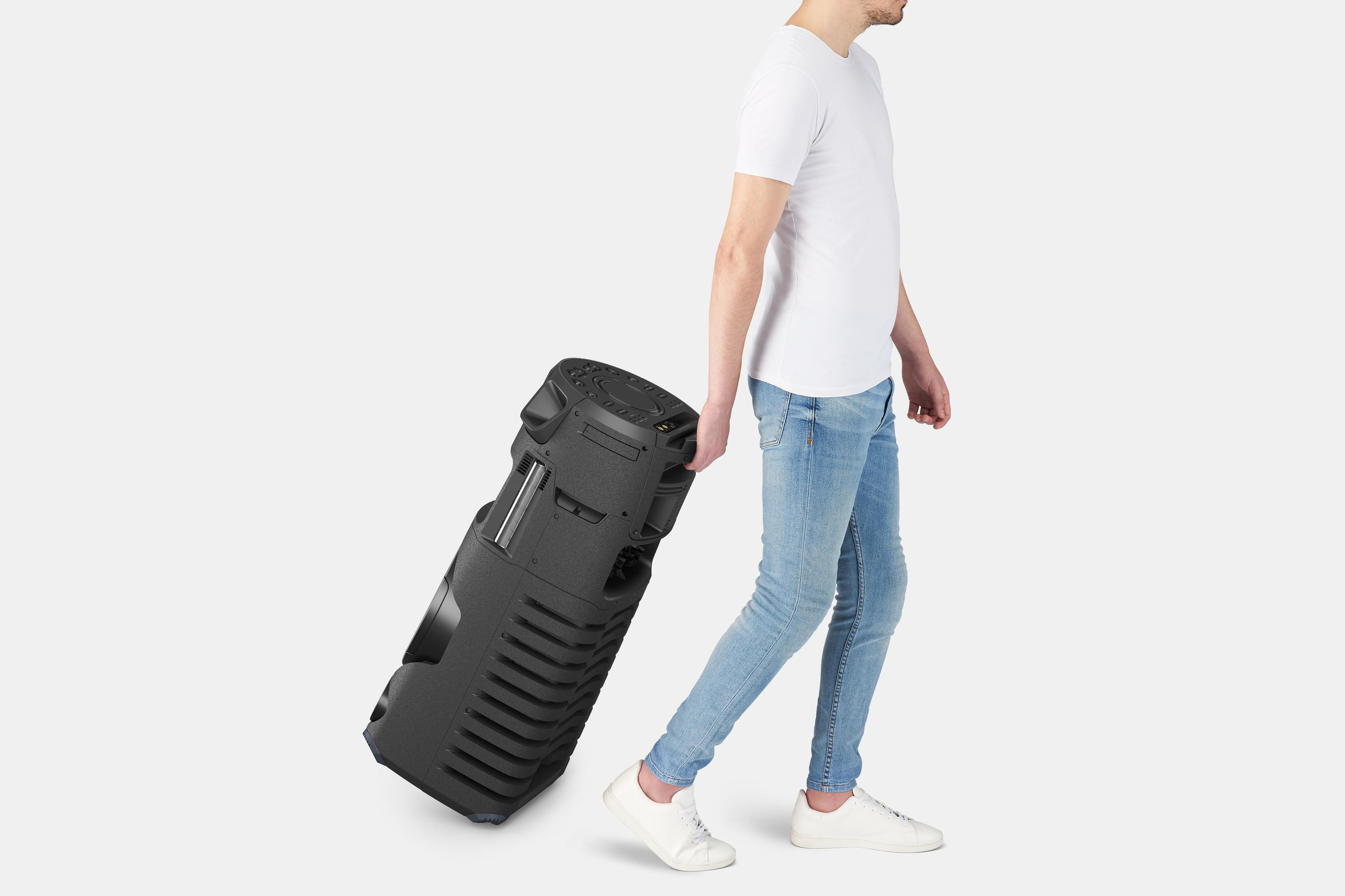 Ein Mann in weißem T-Shirt und Jeans zieht einen großen schwarzen Lautsprecher auf Rädern.