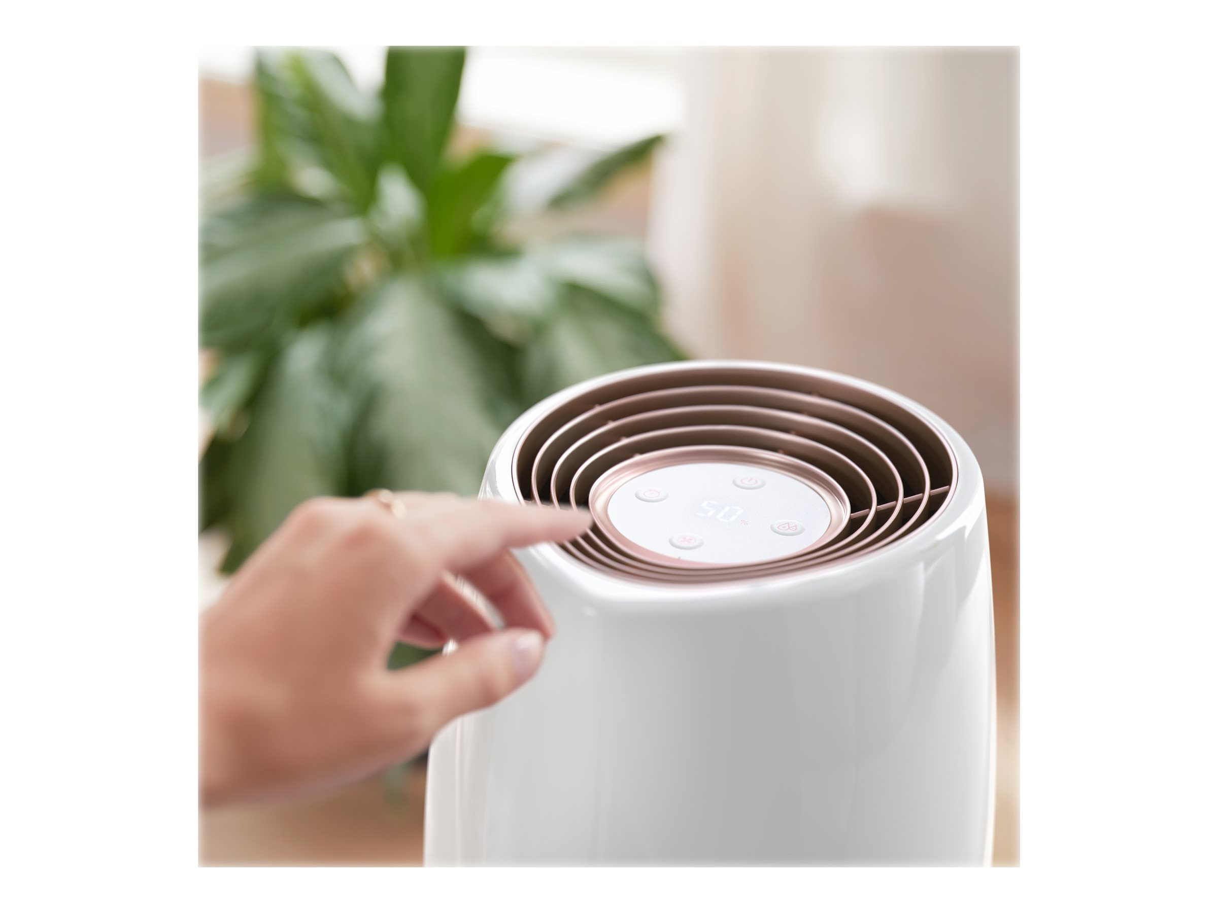 Humidificateur blanc avec un doigt sur le panneau de commande tactile et une plante verte.