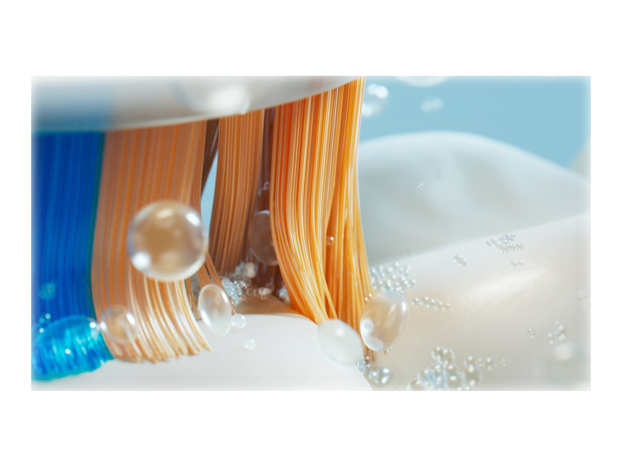 Nahaufnahme eines Zahnbürstenkopfes mit orangefarbenen und blauen Borsten. Blasen drumherum.