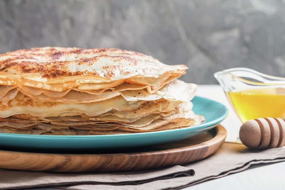 Arany palacsinták halmaza kék tányéron, sziruppal és mézcsurgatóval.