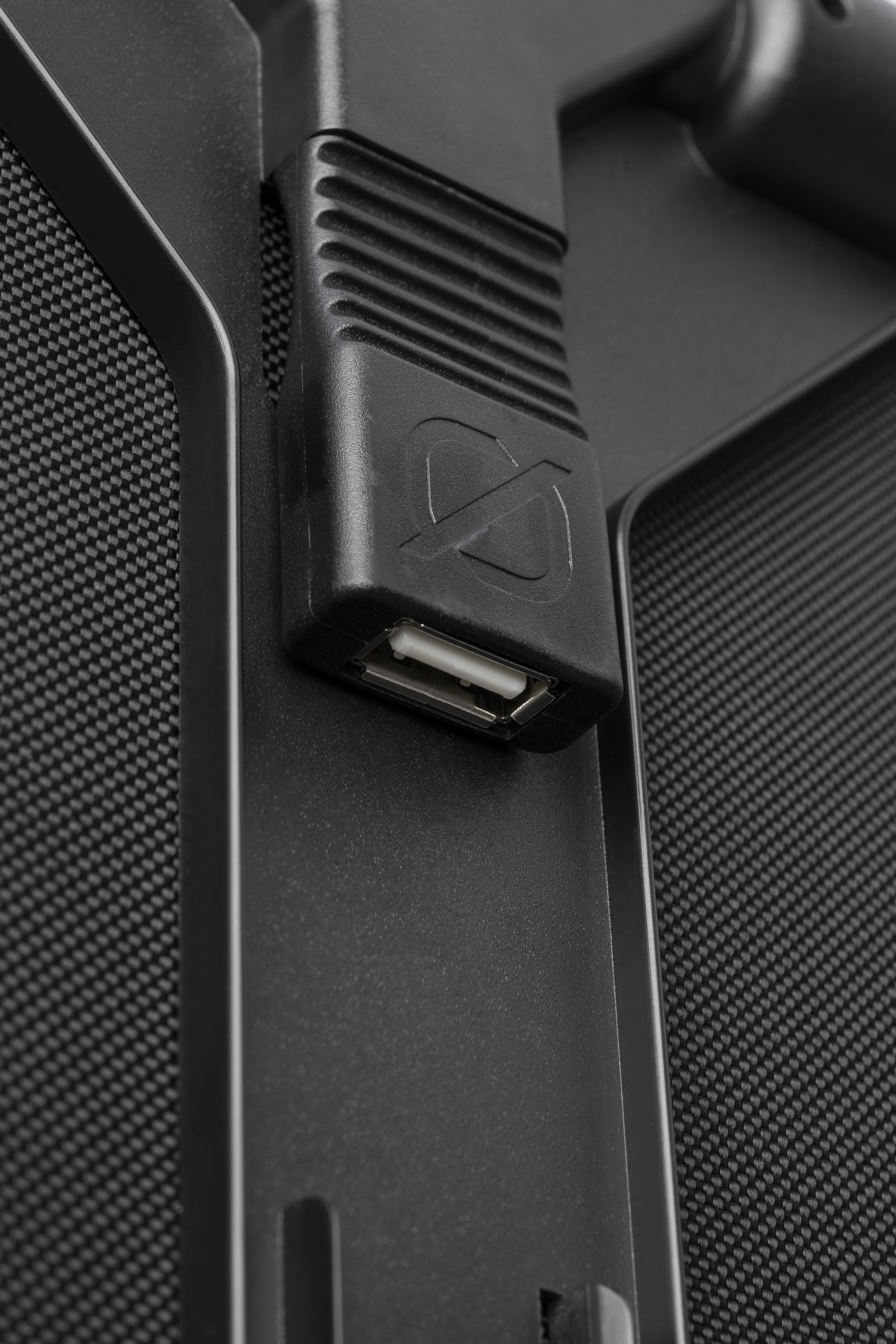 Nahaufnahme eines schwarzen USB-Anschlusses an einem schwarzen Gerät mit strukturiertem Mesh-Hintergrund.