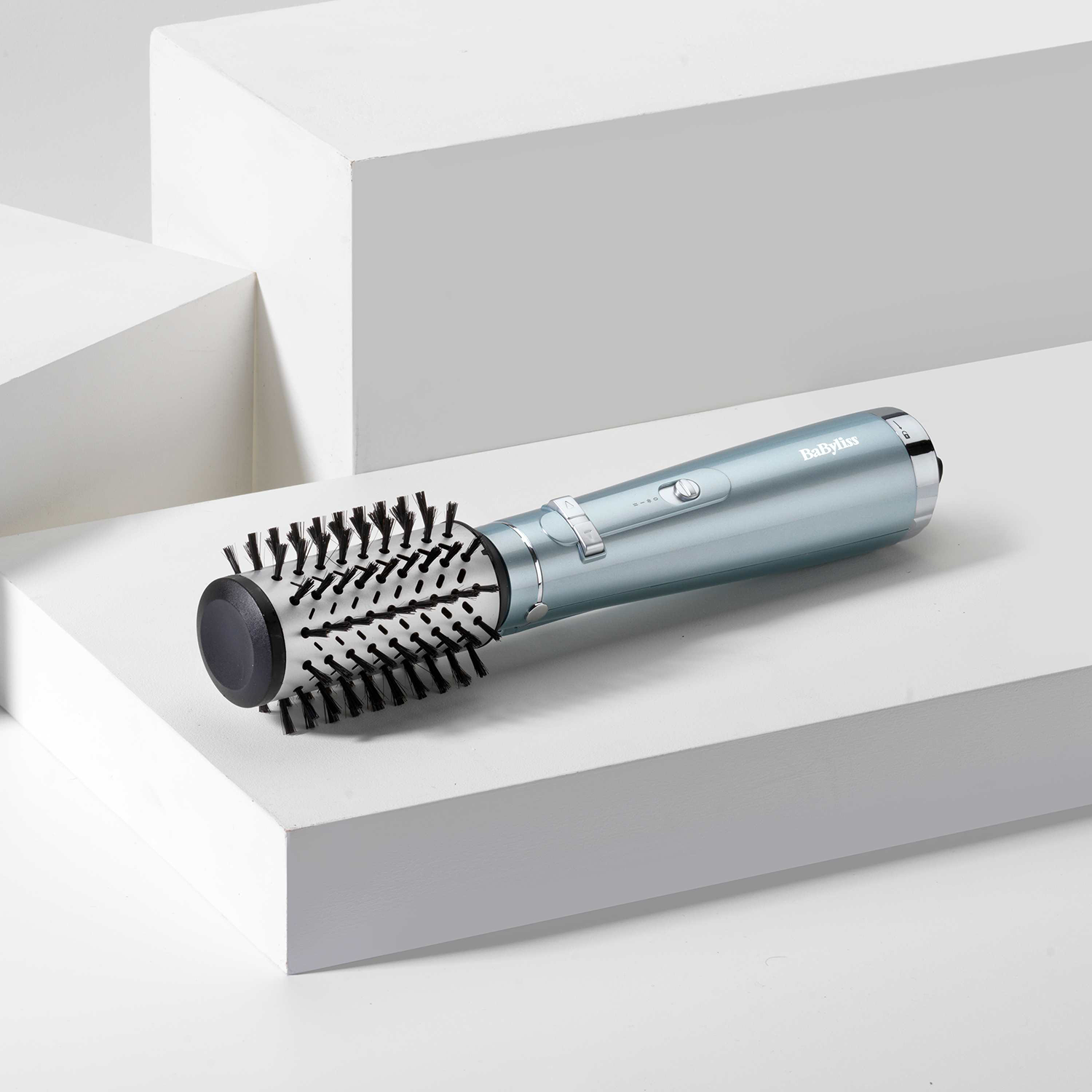 Hair styler, silver and black, on a white geometric surface.