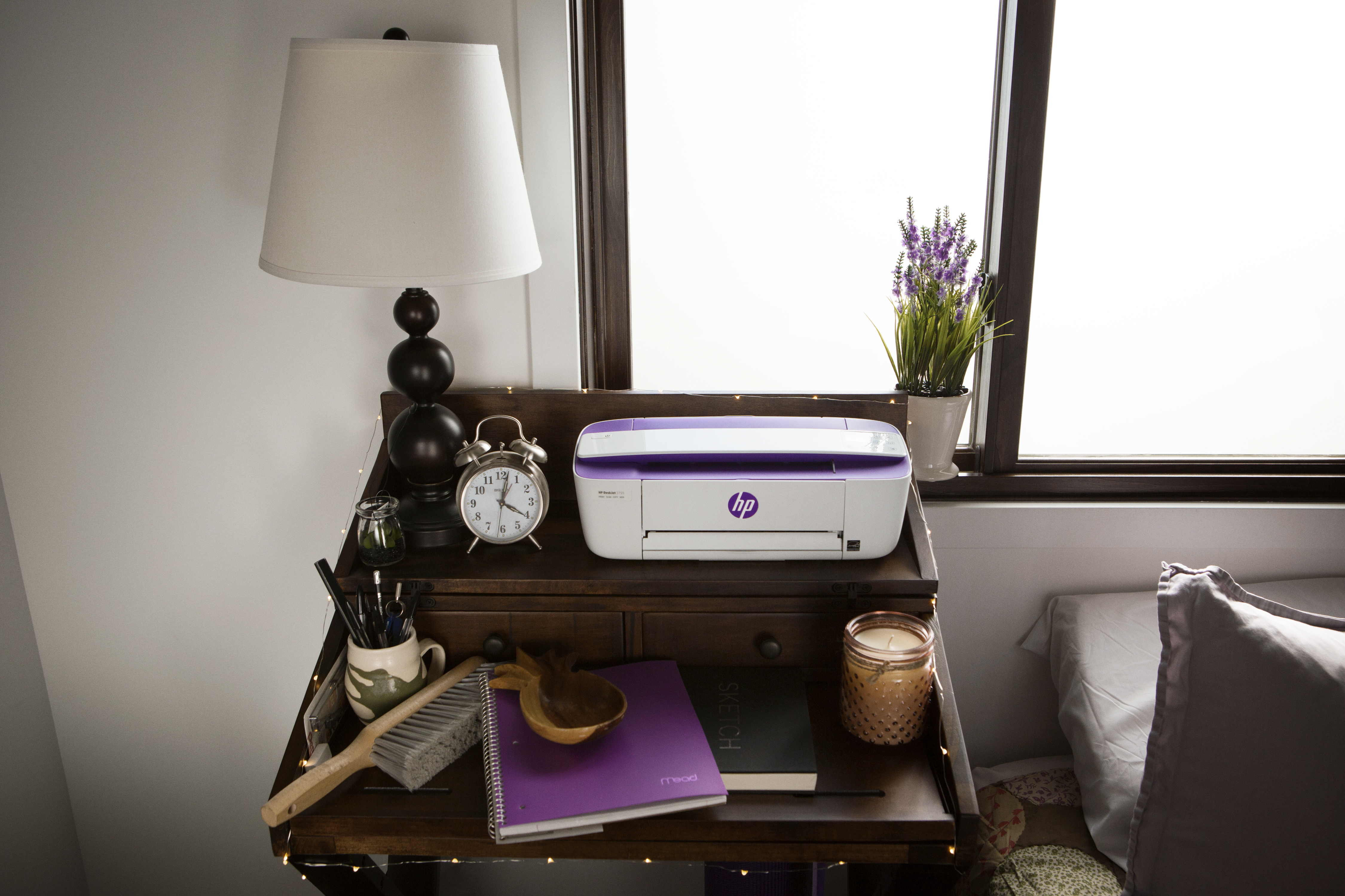 Un escritorio con una lámpara, una impresora y otros útiles de oficina, junto a una ventana.