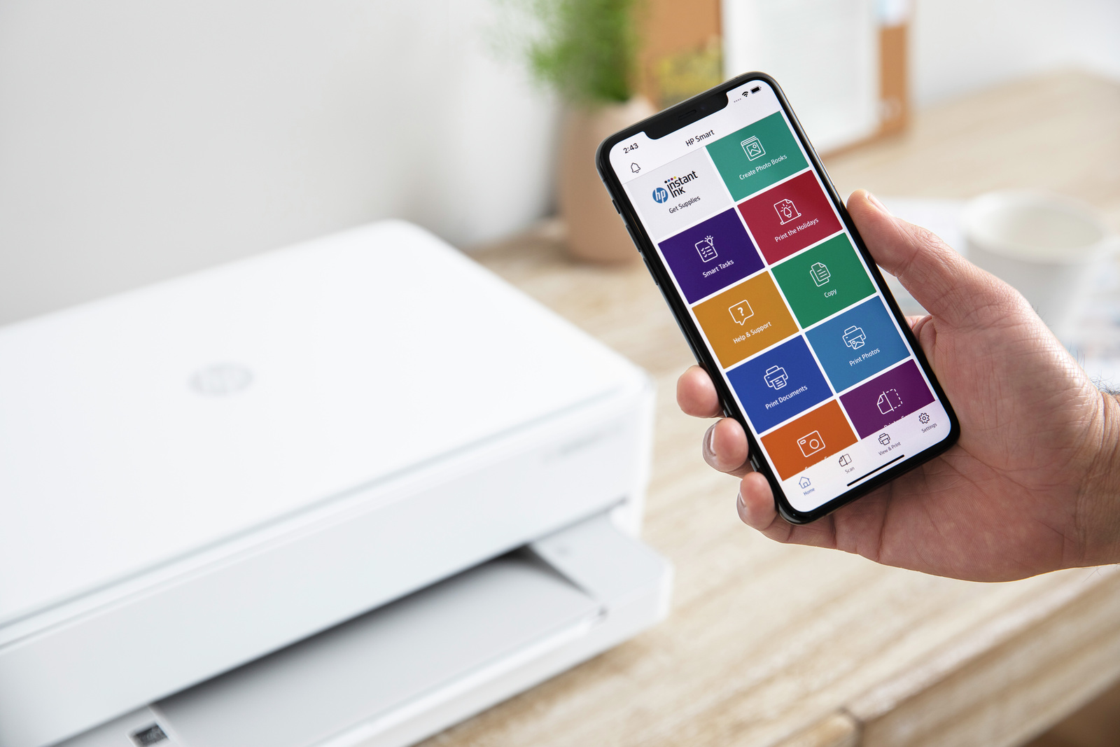 Persona sosteniendo un smartphone que muestra la interfaz de la aplicación HP Smart frente a una impresora.