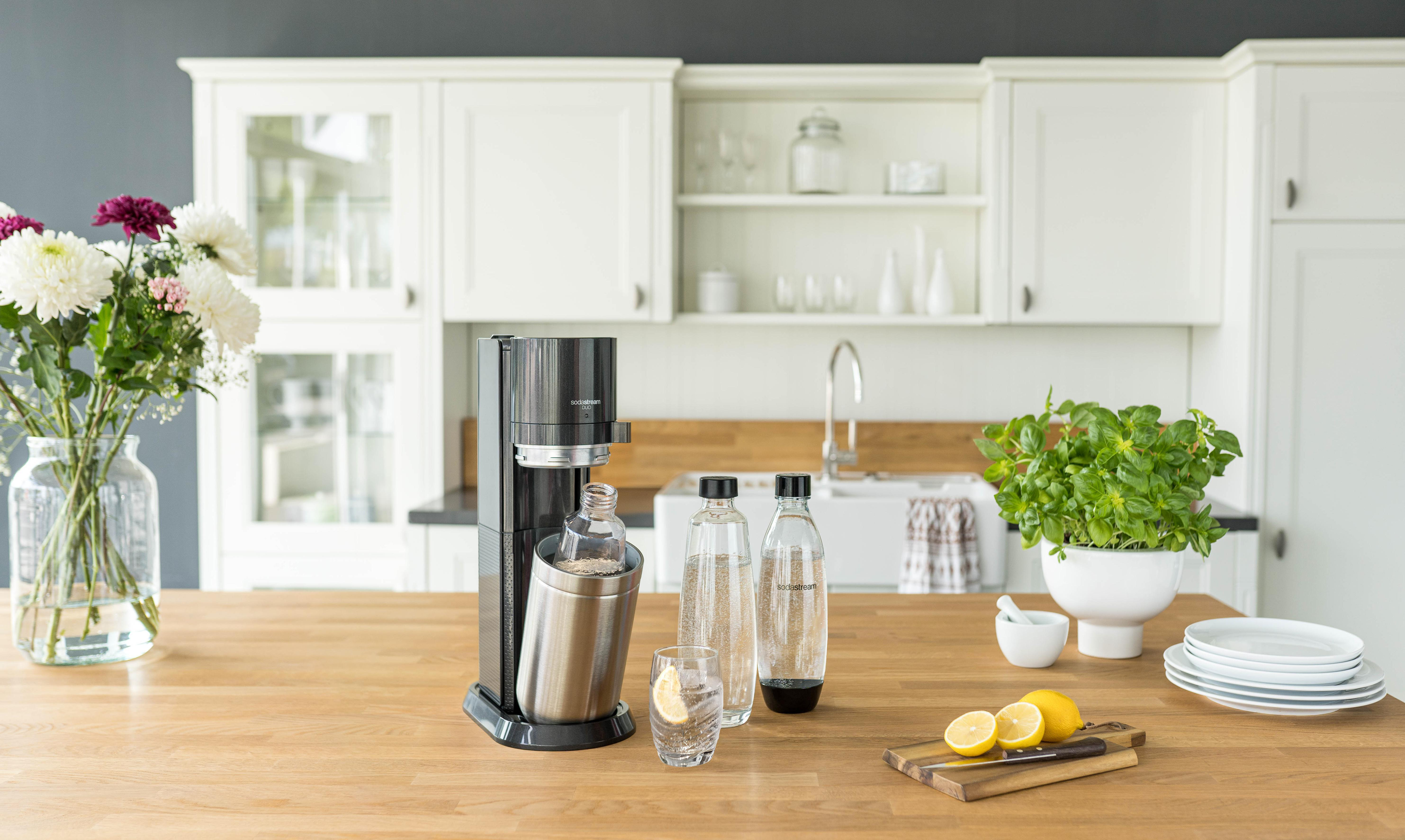 Küchenszene: Soda-Maker, Wasserflaschen, Zitronen und Blumen.