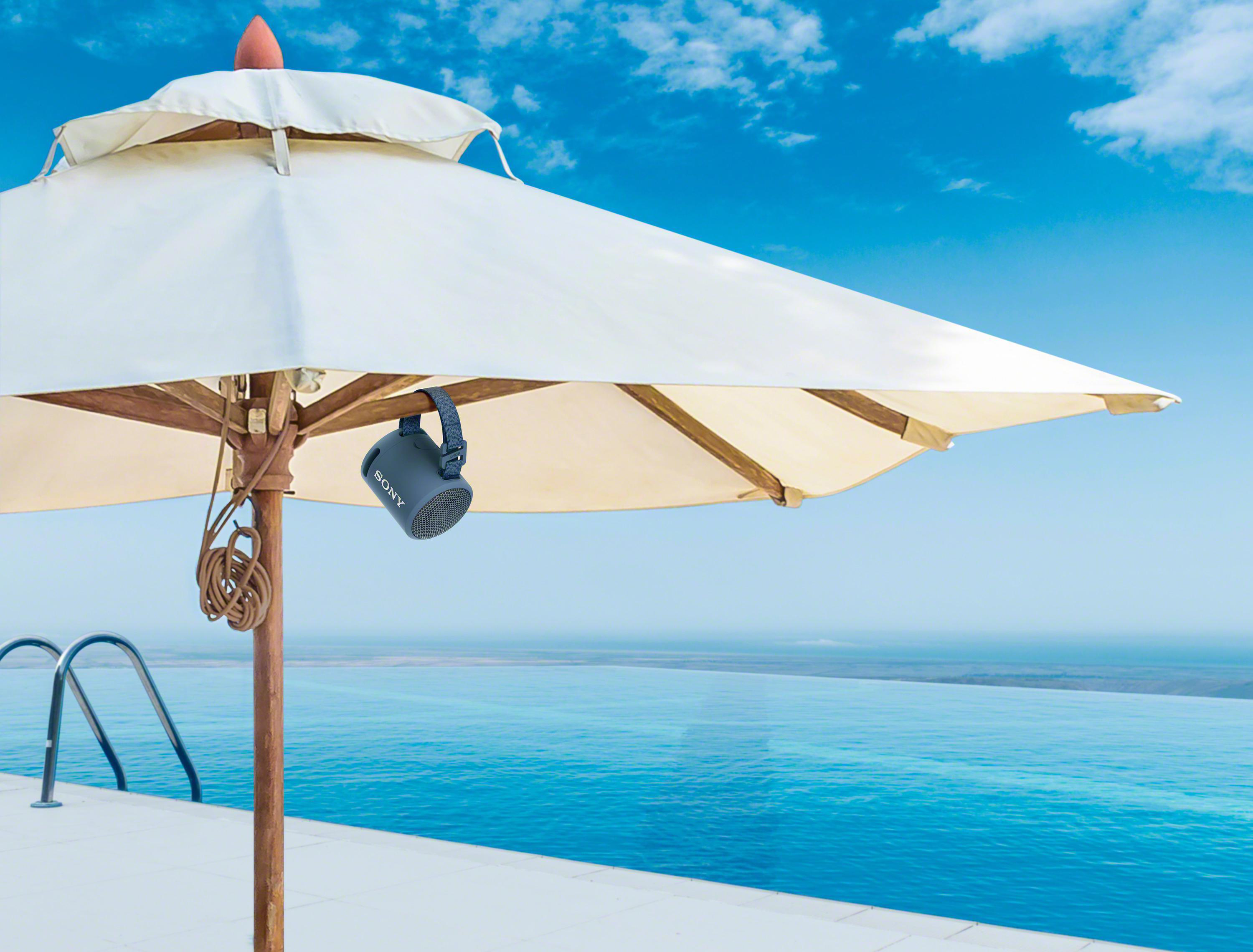Ein Lautsprecher hängt an einem Regenschirm über einem Pool und dem Meer.