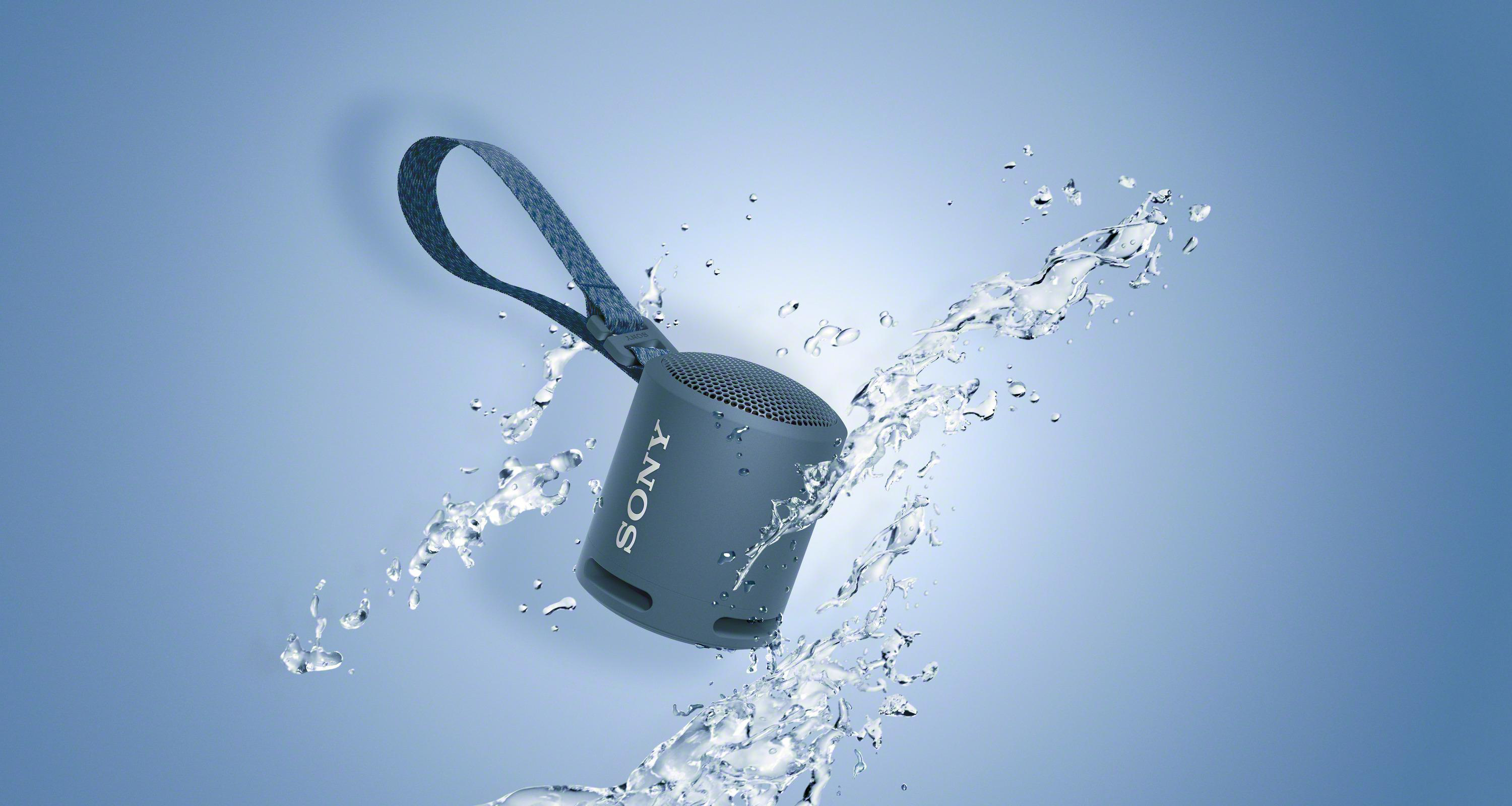 Grauer Sony-Lautsprecher, Wasser spritzt herum, mit blauem Farbverlauf im Hintergrund.