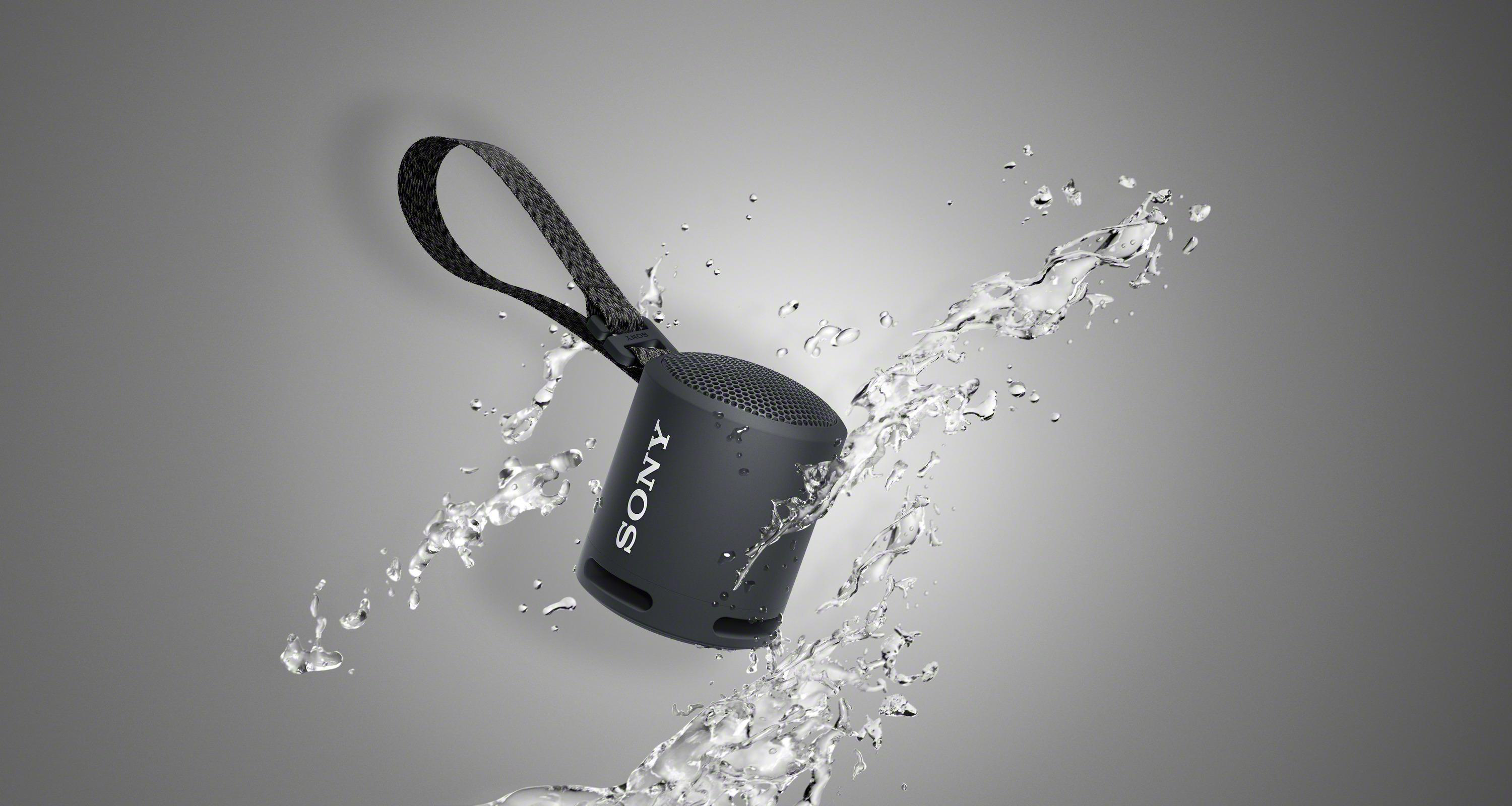Ein kleiner schwarzer Sony-Lautsprecher mit Riemen, spritzendes Wasser. Grauer Hintergrund.