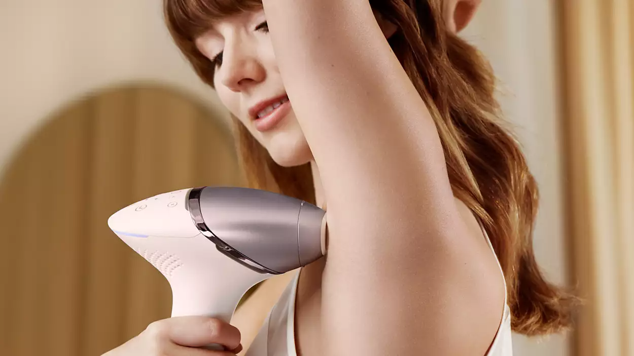 A woman using a white Philips hair removal device on her armpit.