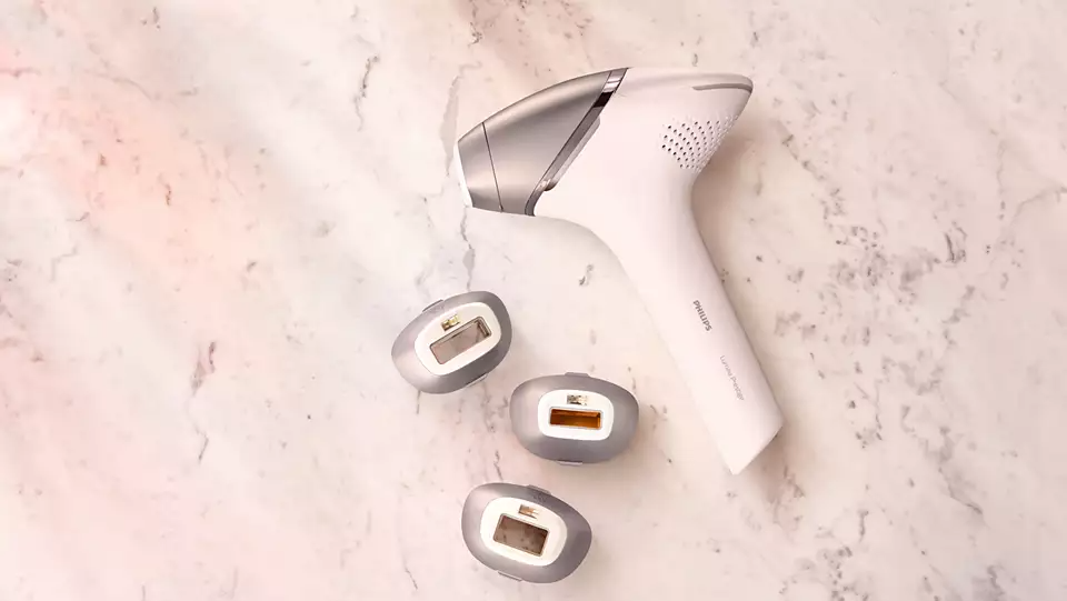 A white and silver Philips hair removal device with three replacement heads on a marble surface.