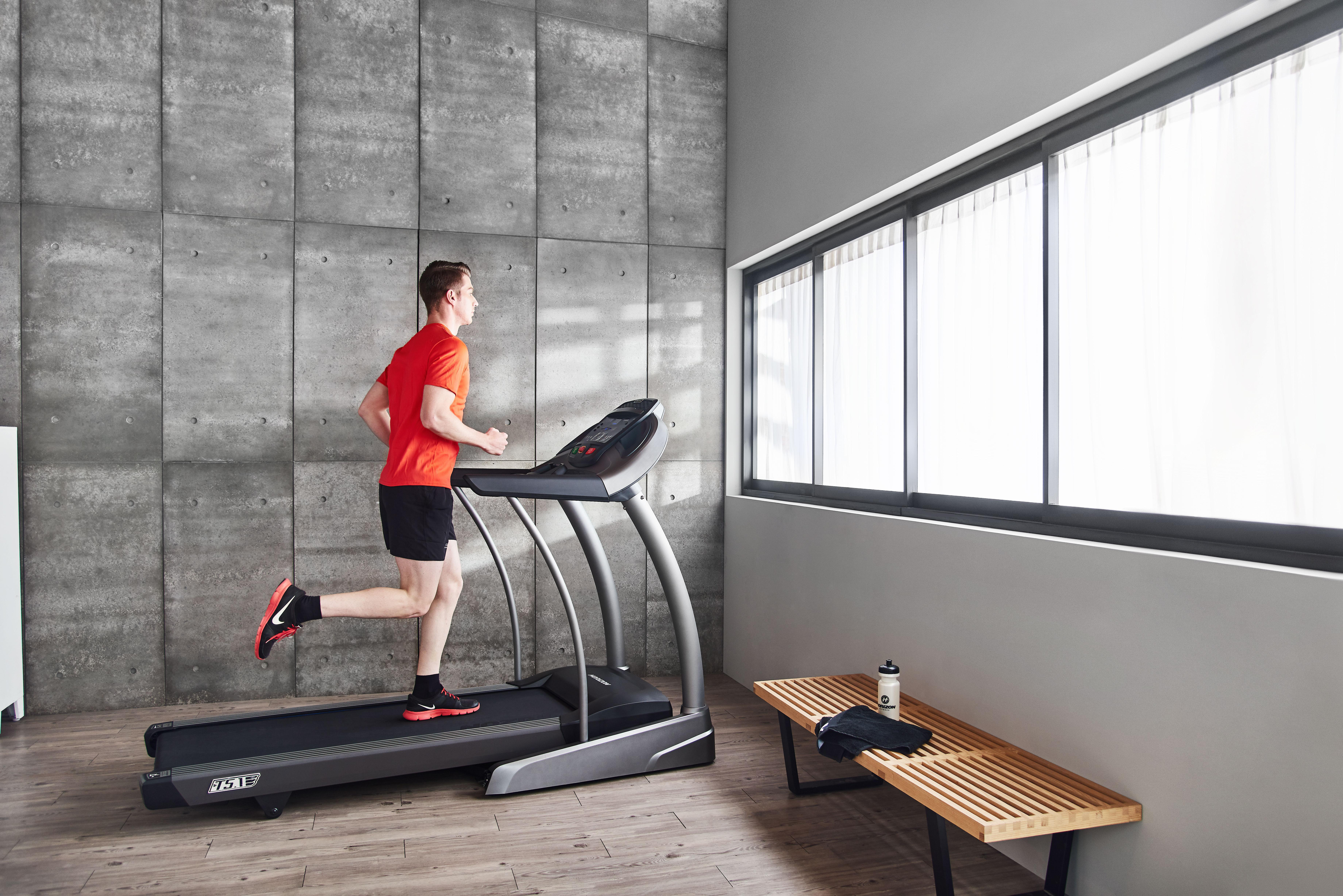 Mann, der in einem Fitnessstudio auf einem Laufband läuft, in der Nähe eines Fensters.