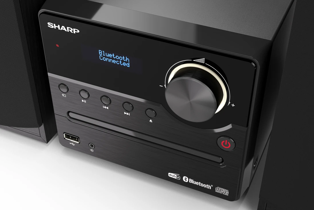Fekete sztereó rendszer, a kijelzőn a „Bluetooth csatlakoztatva” felirat látható. Hangerő gomb és gombok láthatók.