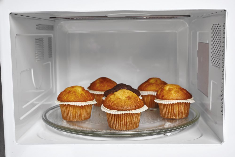 Dentro de un microondas: seis muffins en un plato de vidrio, listos para calentar.