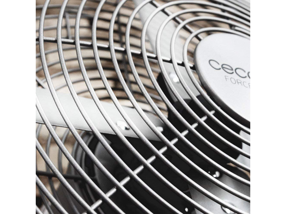 Vista de cerca de la rejilla metálica de un ventilador. El ventilador es plateado y el fondo borroso.