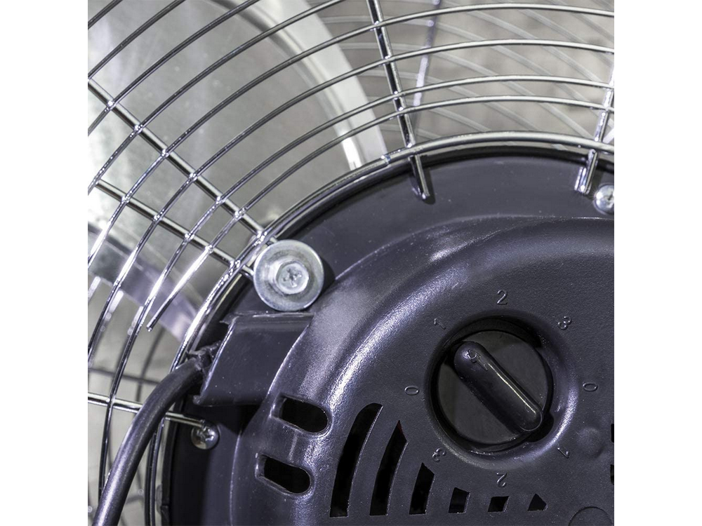 Primer plano de la parte trasera de un ventilador plateado con carcasa del motor negra y cable.
