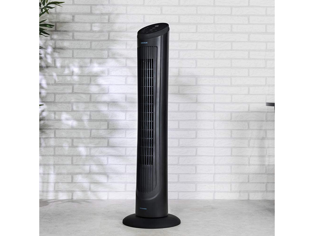 Ventilador de torre negro frente a una pared de ladrillos blancos. Una planta en el suelo.