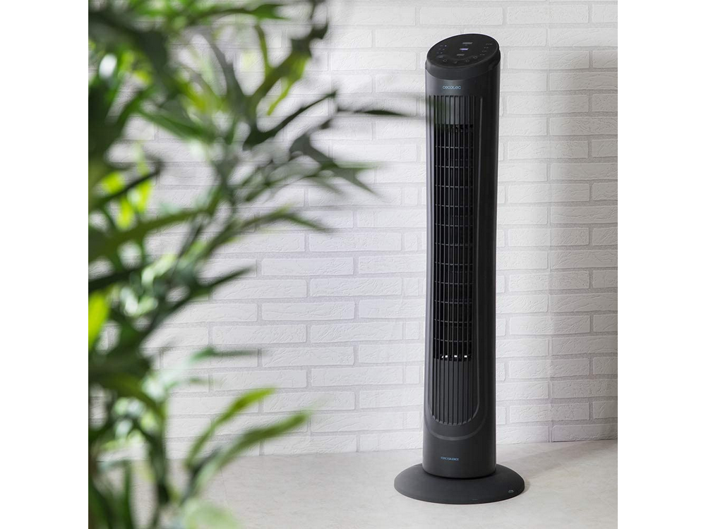 Un ventilador de torre negro sobre una mesa, con un fondo de pared de ladrillos blancos.