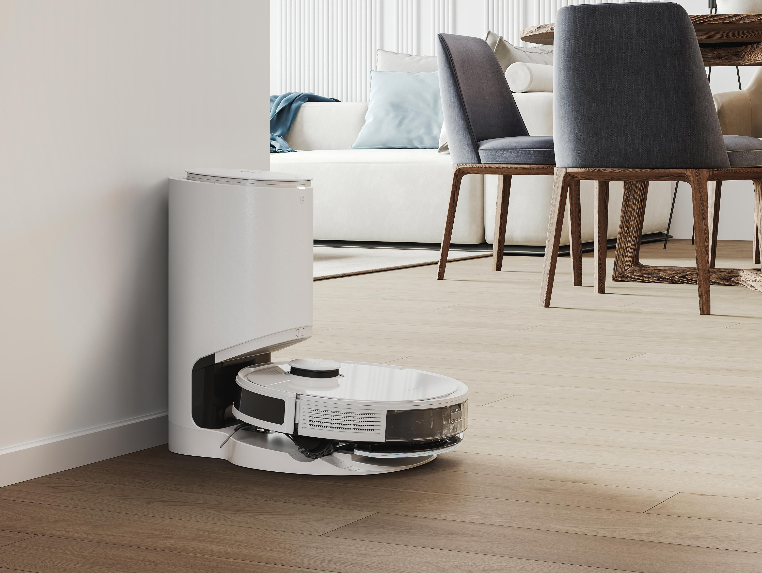Weißer Roboter-Staubsauger und Dockingstation, Holzboden, weiße Wand, Sofa und Stühle.