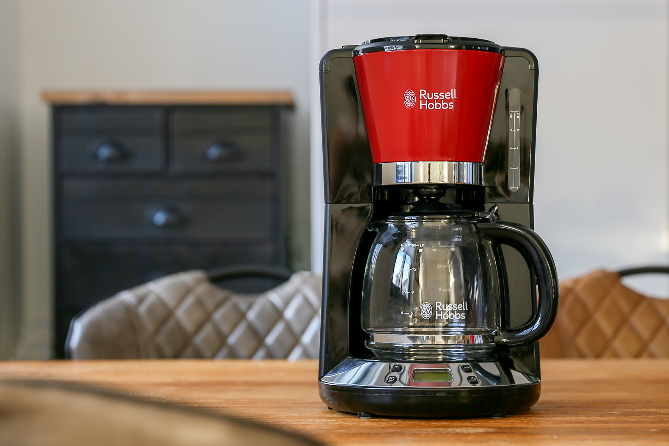 Coffee maker on a wooden table. Black and red design, glass carafe visible.