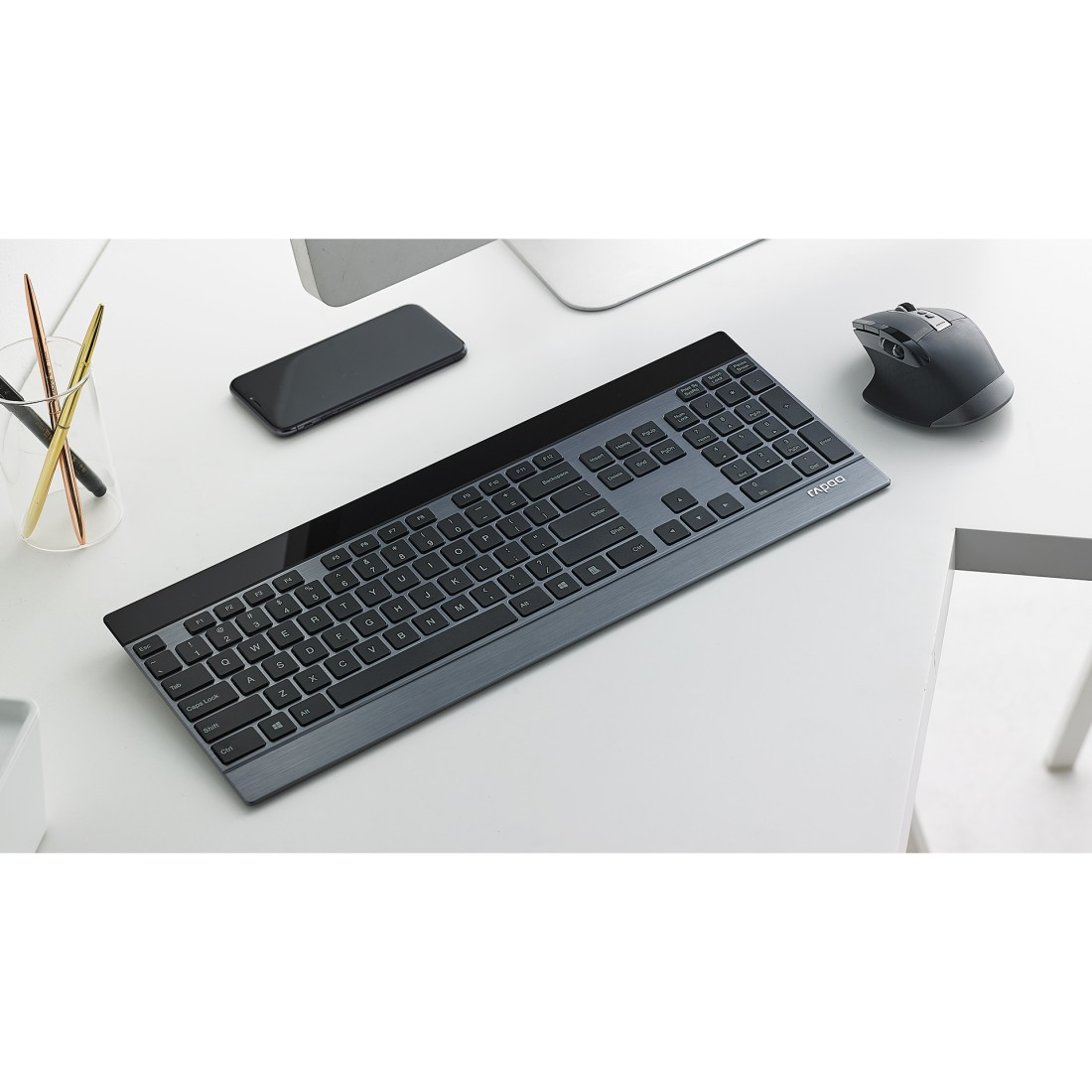 Tastatur, Telefon und Maus auf weißem Schreibtisch. Goldener Stift im Glas.