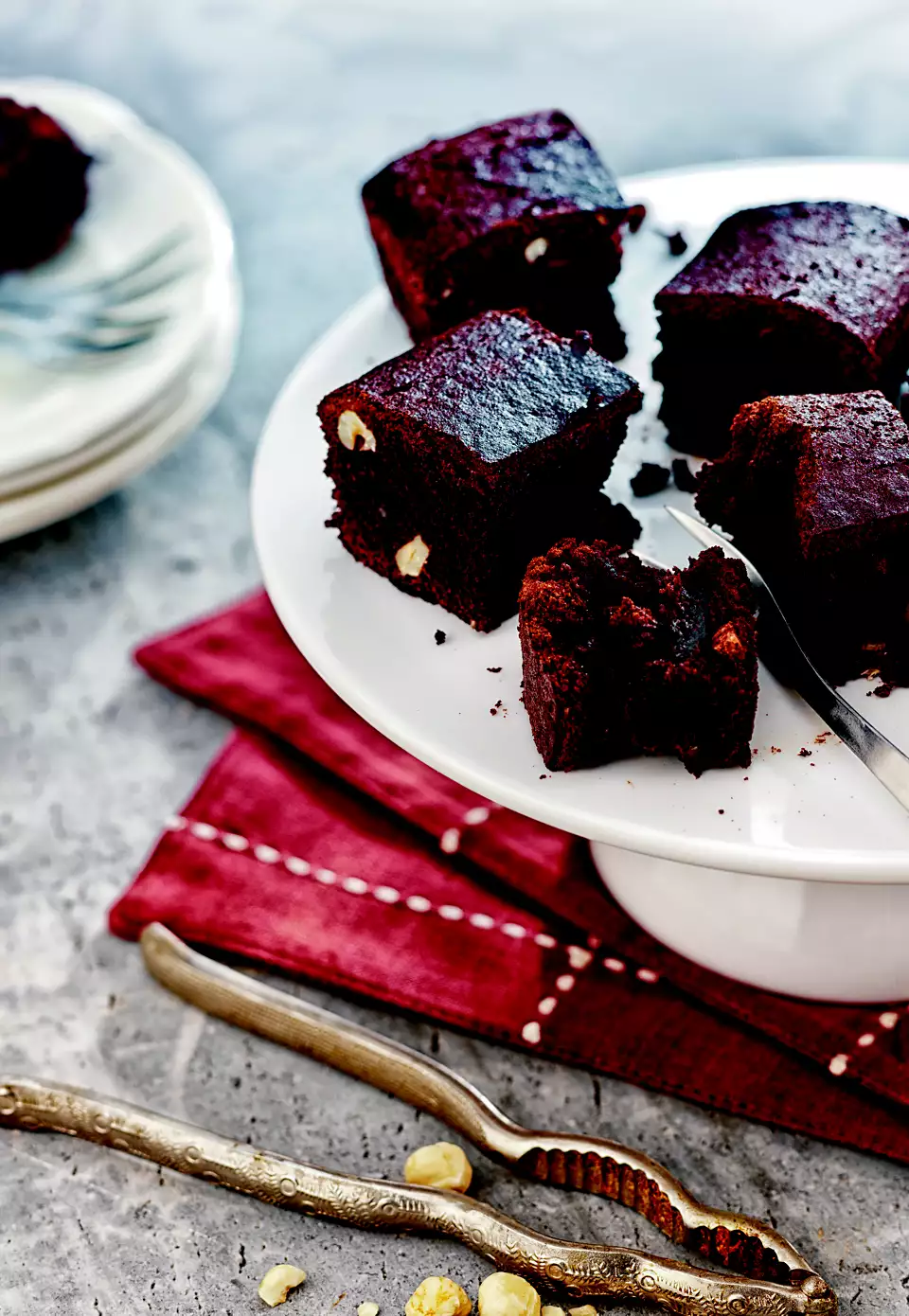 Quadratini di brownie su un piatto a piedistallo bianco, con un tovagliolo rosso e uno schiaccianoci in primo piano.