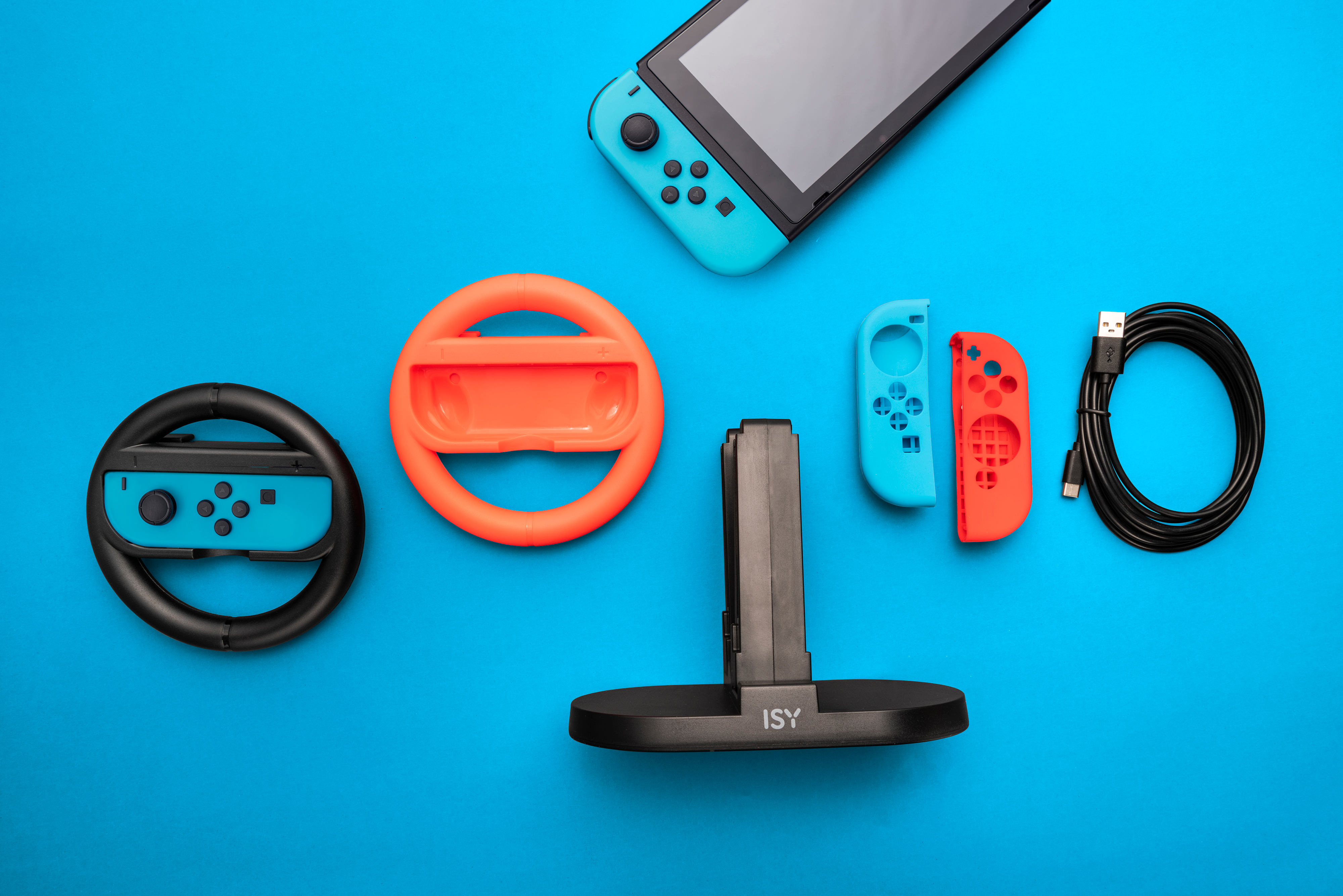 Accessori Nintendo Switch: console, volanti, controller e supporto di ricarica su superficie blu.