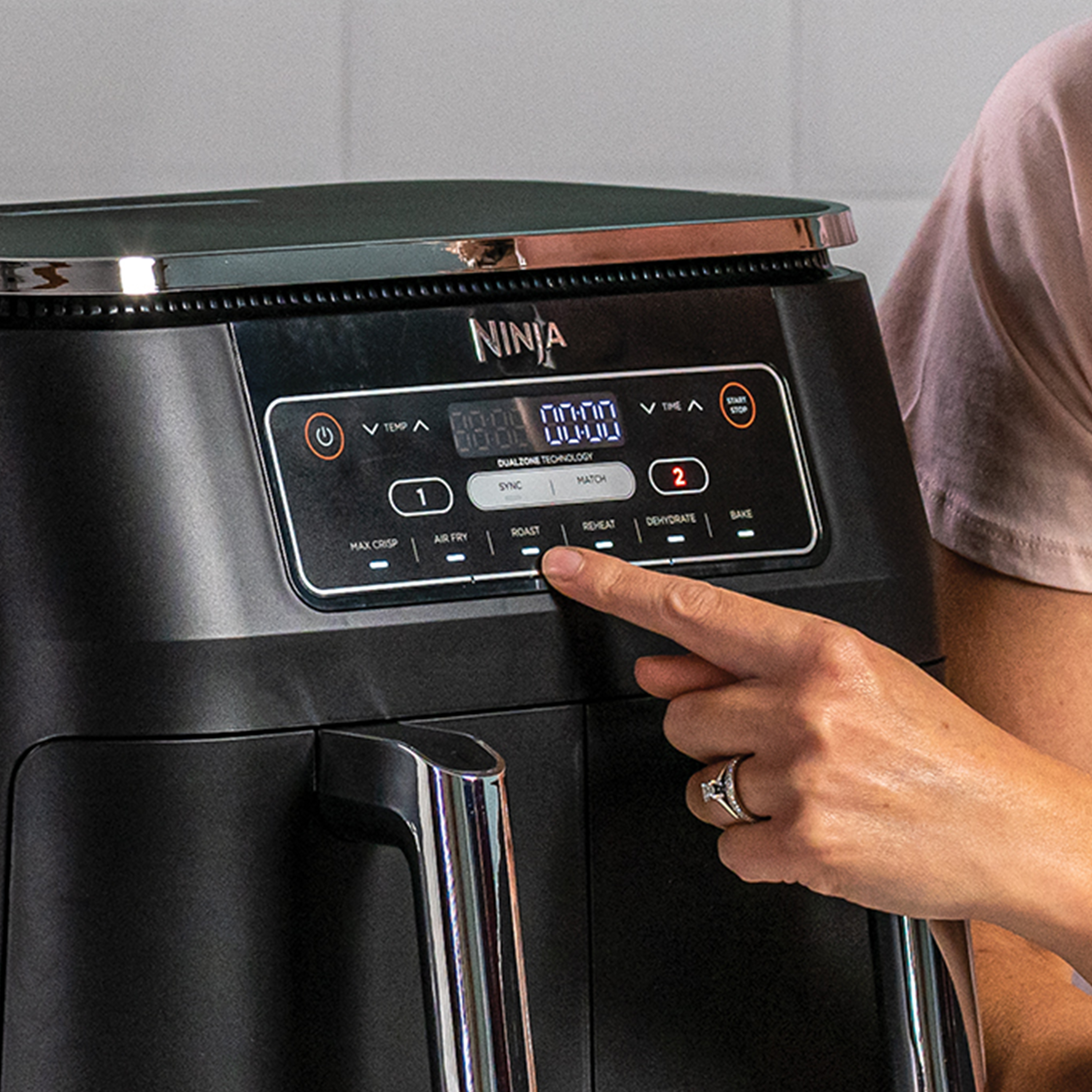 Zwarte Ninja airfryer. Hand drukt op knop. Zwarte achtergrond.